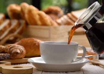 Pouring coffee with smoke on a cup with breads or bun, croissant and bakery on white wooden table
